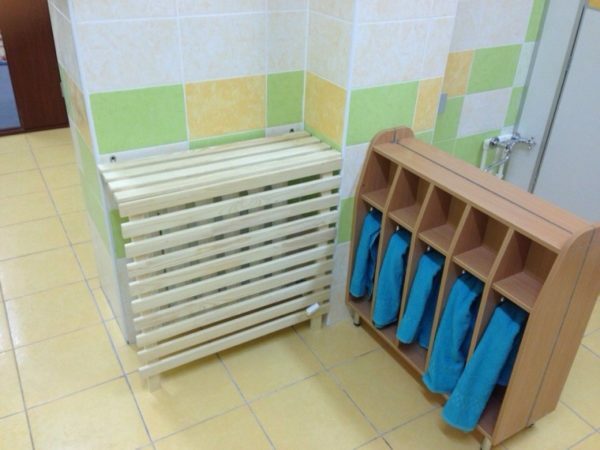 Bathroom in the kindergarten. Wooden shield protects children from burns when in contact with the battery.