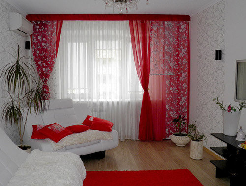 Red curtains in conjunction with cushions and a carpet of the same color made monochromatic living room festive and bright